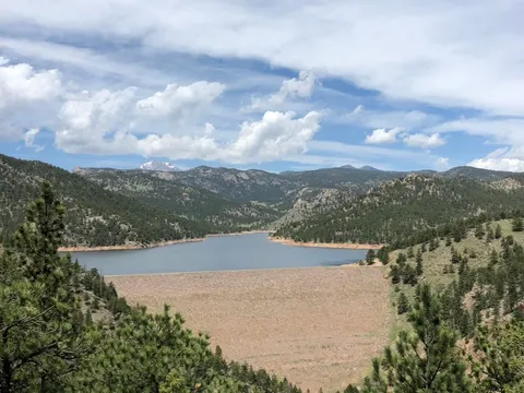 The dam and reservoir at Button Rock Preserve above Lyons, forested hills on either side and snow still on the peaks beyond