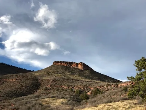 The flat-topped red sandstone butte at Hall Ranch under a breaking storm, grass and scrub on the slope below it