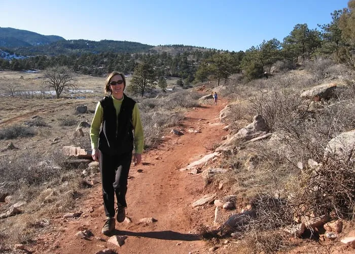 A hiker on the red-dirt Bitterbrush trail at Hall Ranch, sandstone ridge behind