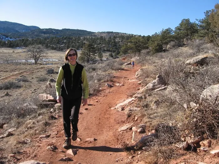 A hiker on the red-dirt Bitterbrush trail at Hall Ranch, sandstone ridge behind