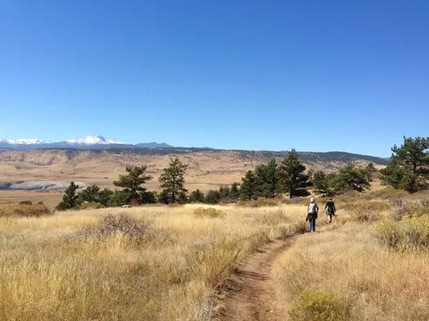 Two walkers on the trail at Rabbit Mountain, dry grass either side and snow on the peaks along the horizon